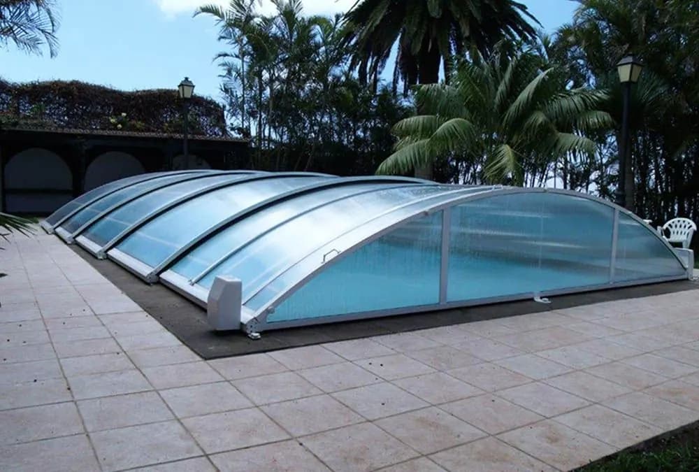 Cubierta telescópica baja translúcida sobre una piscina junto a un jardín